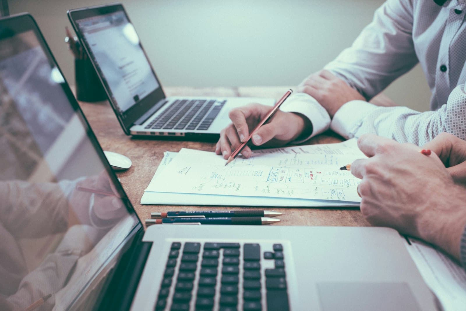Business professionals reviewing financial documents and plans at a desk with laptops in natural light (Photo: Unsplash)