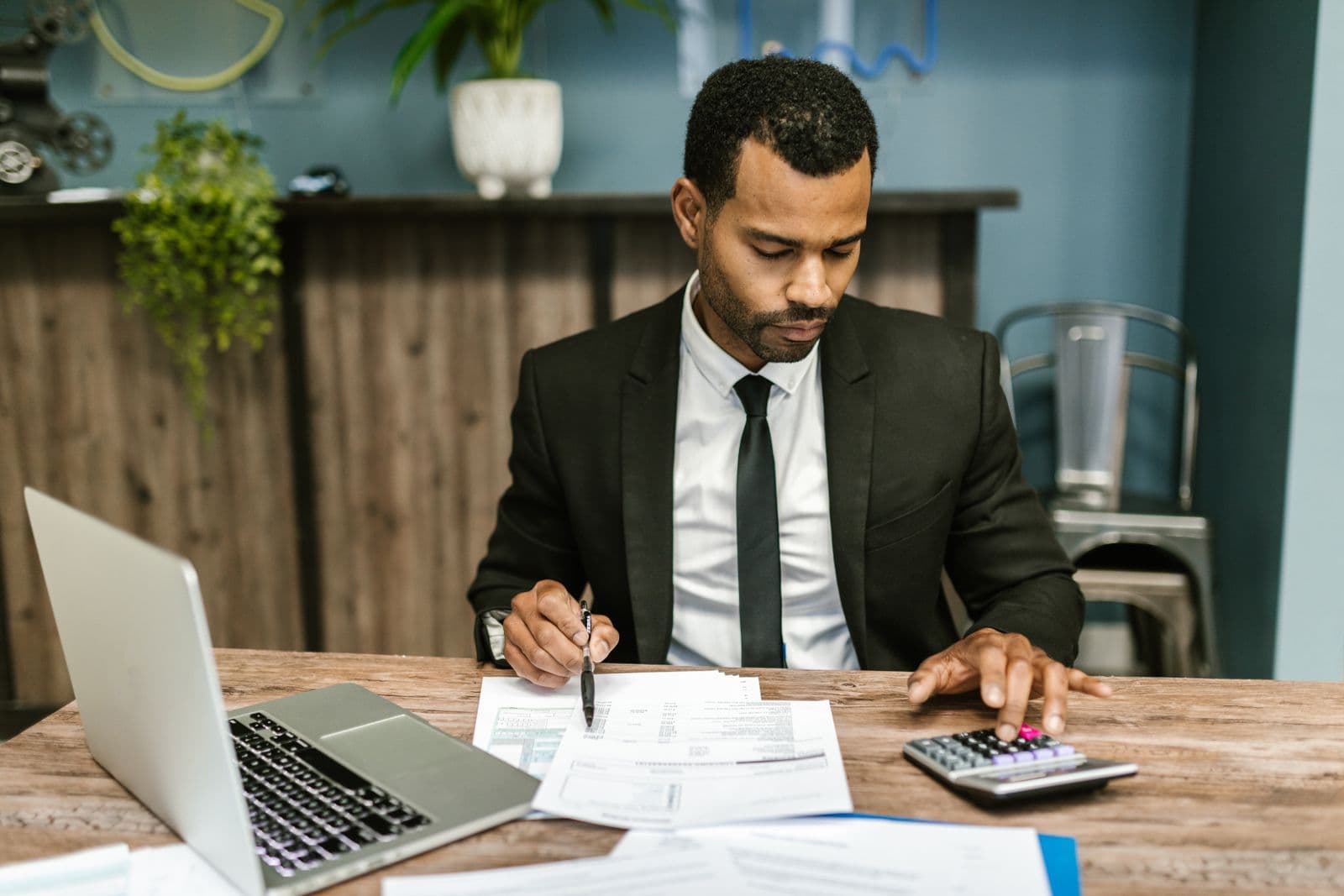Professional reviewing invoices and financial documents at a desk with a laptop and calculator in natural light (Photo: Pexels)