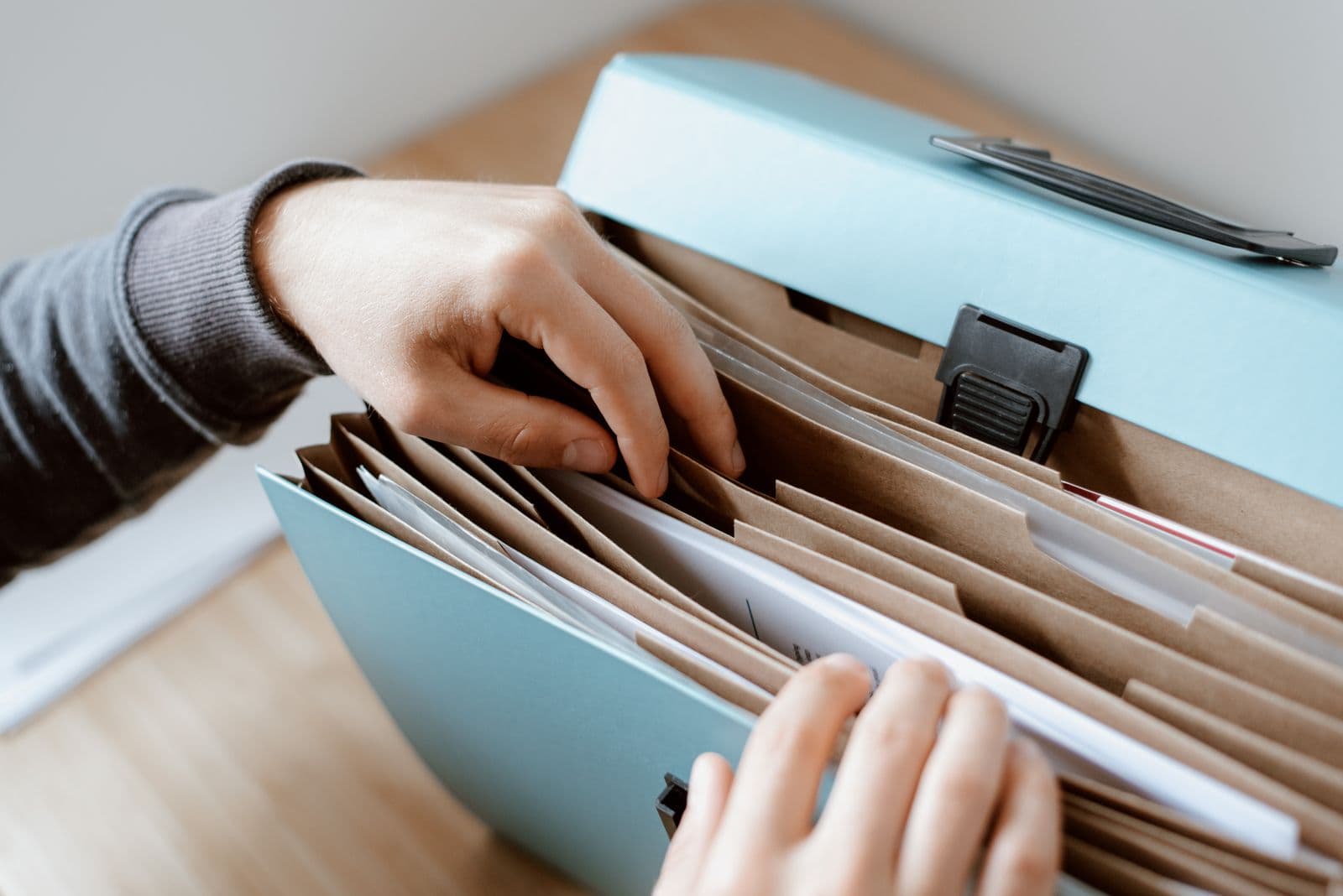 Hands organising documents in a file folder on a wooden desk in natural light (Photo: Pexels)